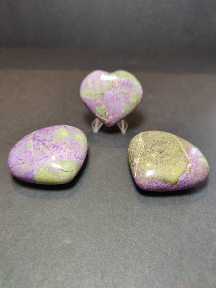 Polished gemstone heart and palmstone sculptures in purple and green on clear stands