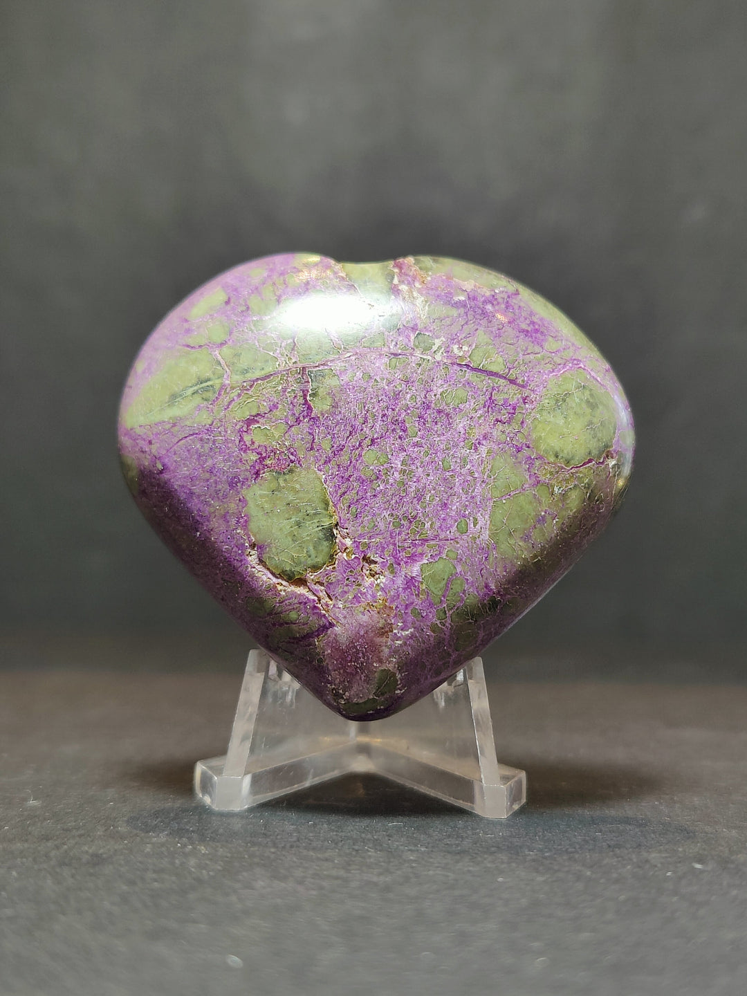Polished purple and green gemstone heart sculpture on clear stand