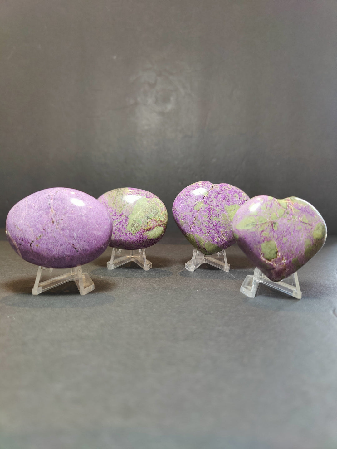 Polished purple and green gemstone heart and palmstone sculptures on clear stands