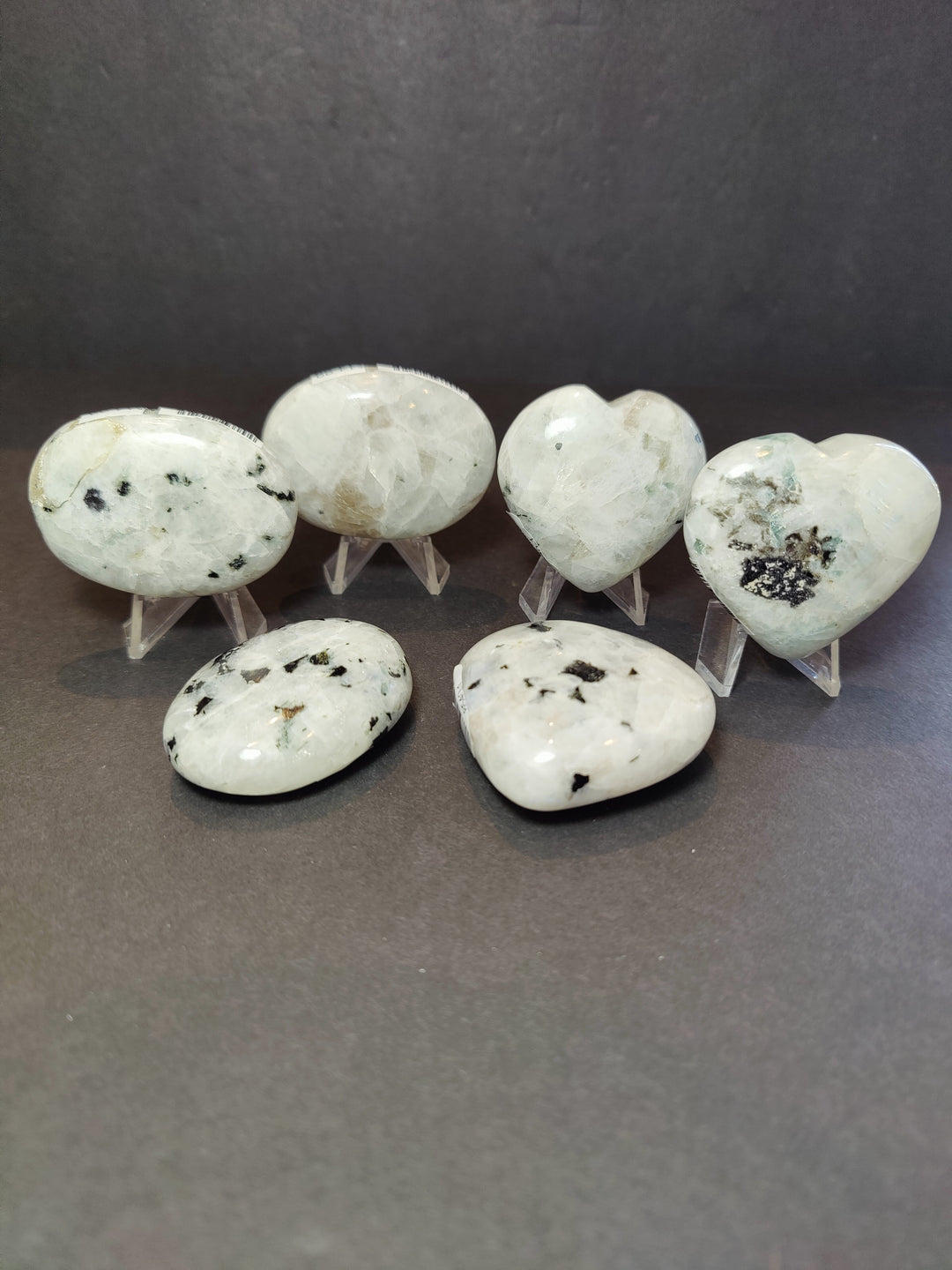 Polished moonstone heart and palmstone sculptures on clear display stands