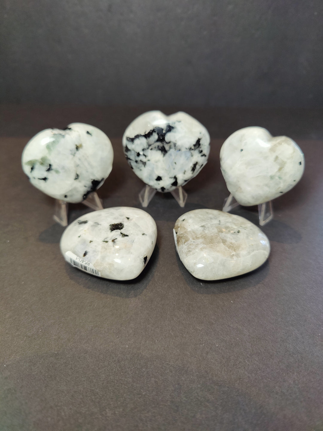 Polished moonstone heart and palmstone sculptures with black mineral specks