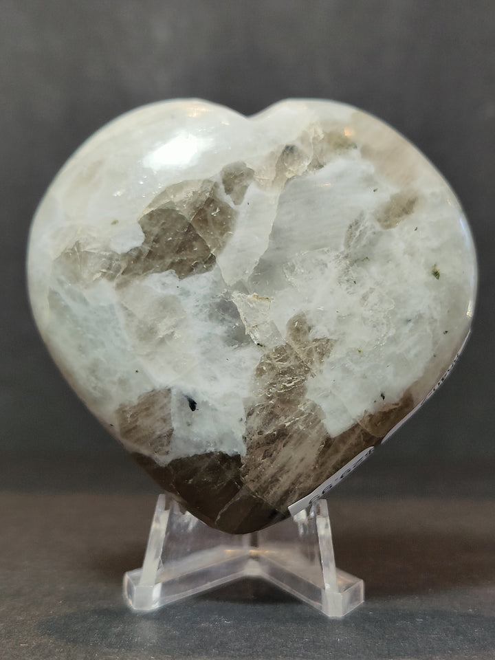 Polished moonstone heart sculpture with natural inclusions on clear stand