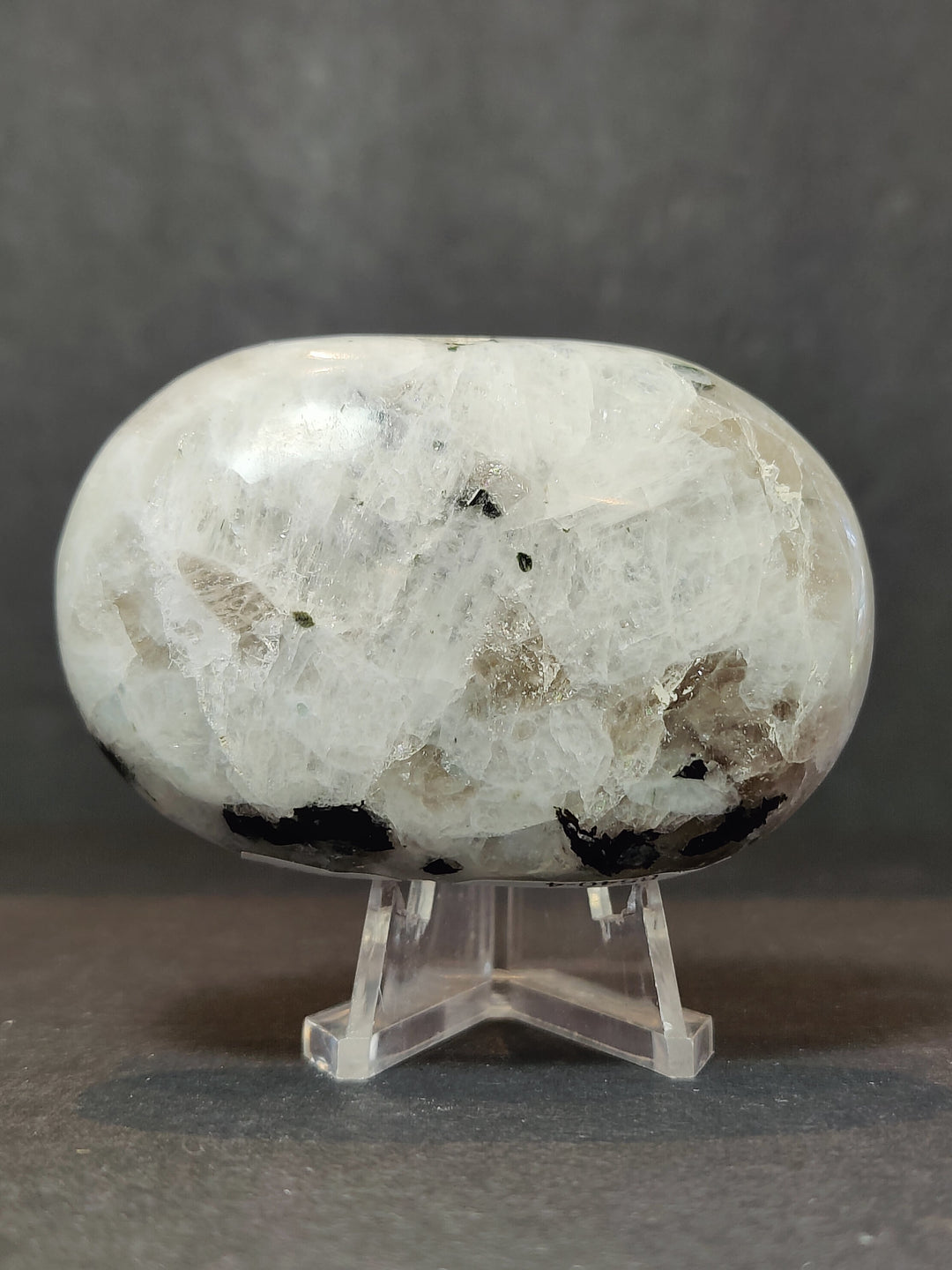 Polished moonstone palmstone sculpture with natural inclusions on clear stand