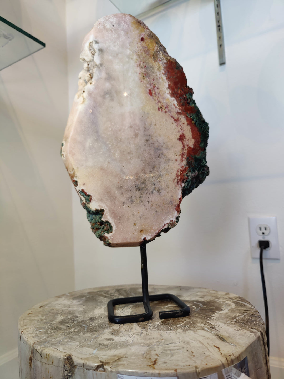 Pink amethyst polished slab on black metal stand over round stone base