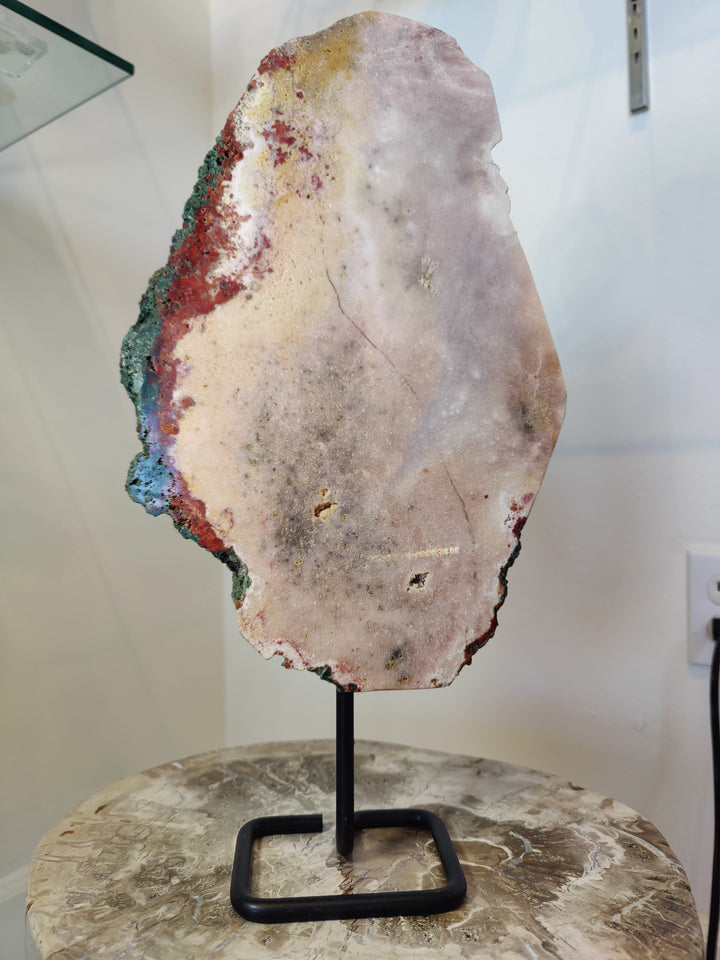 Pink amethyst polished slab with colorful mineral banding on black metal display stand