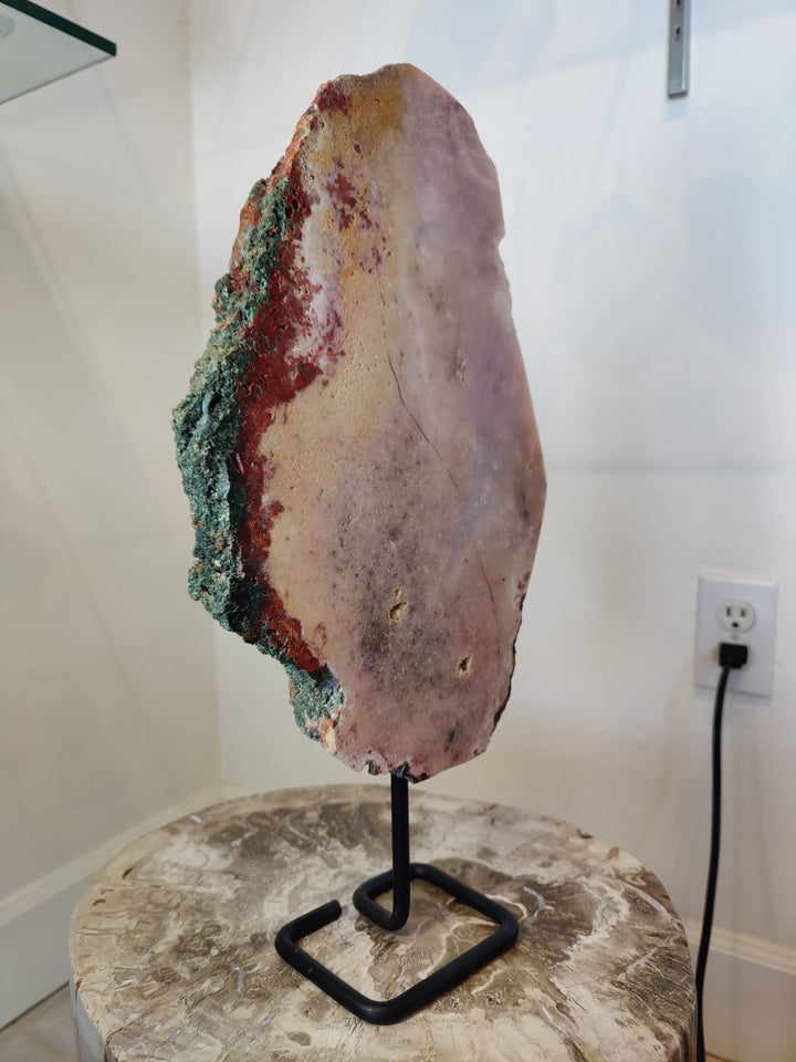 Pink amethyst slab with red underside and green crystal edge on black metal stand