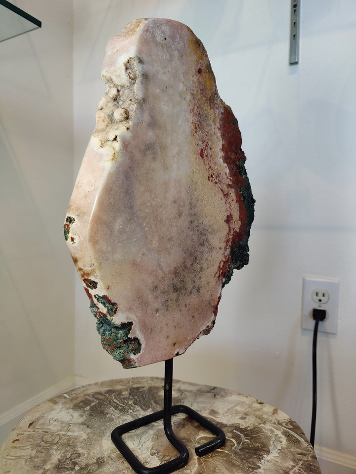Pink amethyst slab sculpture with multicolor mineral rim on black metal display stand