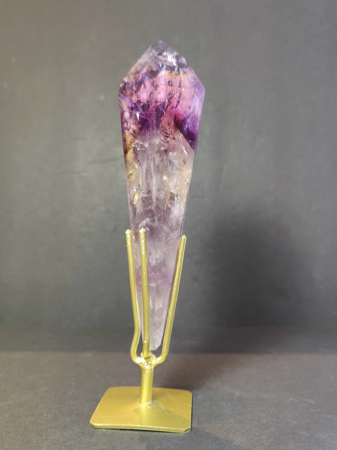 Single amethyst crystal scepter wand on gold metal stand, upright purple point