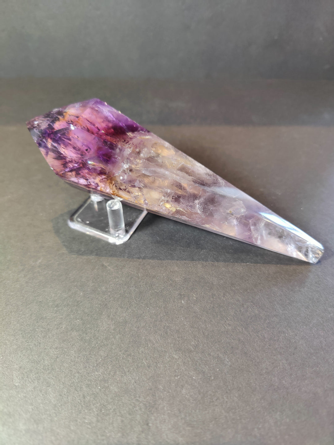 Amethyst crystal scepter wand lying on clear metal stand, purple tip