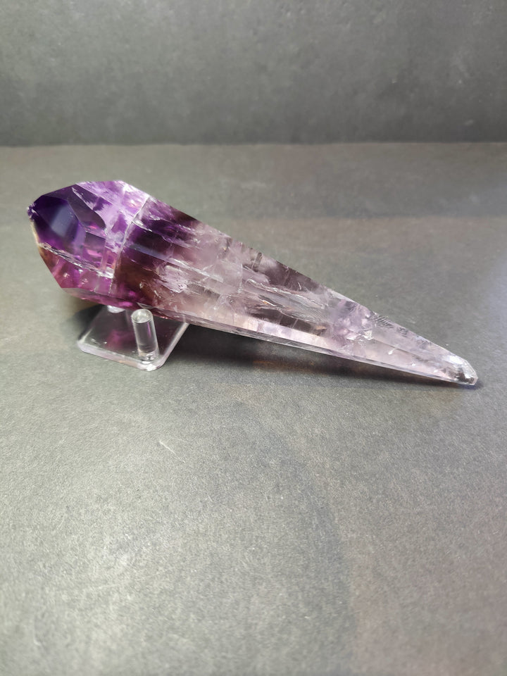 Amethyst crystal scepter wand lying on clear metal stand, purple faceted point