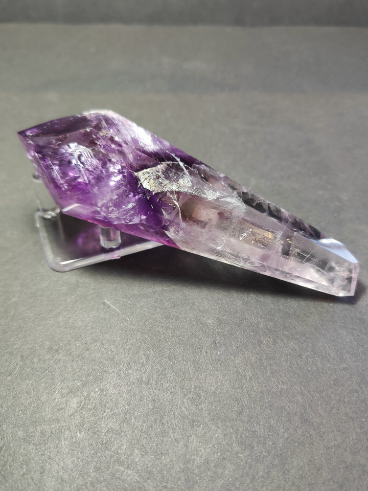 Amethyst crystal scepter wand lying on clear metal stand, purple and clear body