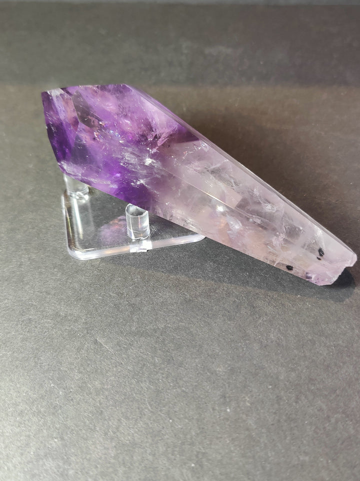 Amethyst crystal scepter wand lying on clear metal stand, long purple crystal