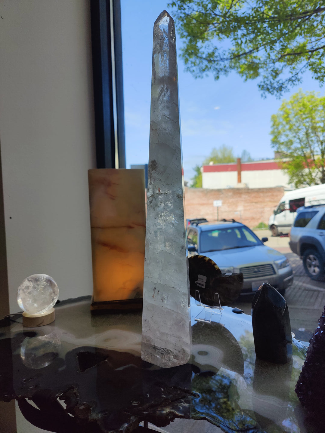 Polished clear quartz obelisk sculpture with clear facets on glass tabletop base