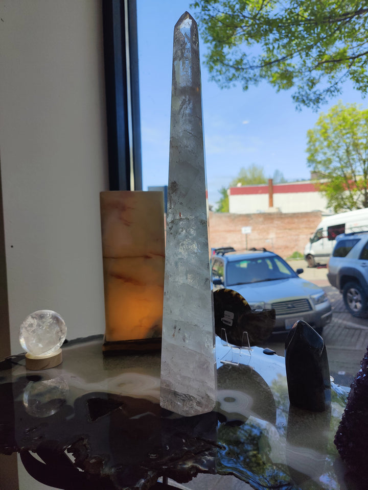 Polished clear quartz obelisk sculpture with clear facets on glass tabletop base