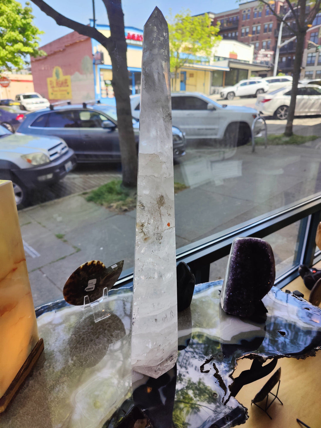 Polished clear quartz obelisk sculpture on dark base, tall transparent crystal