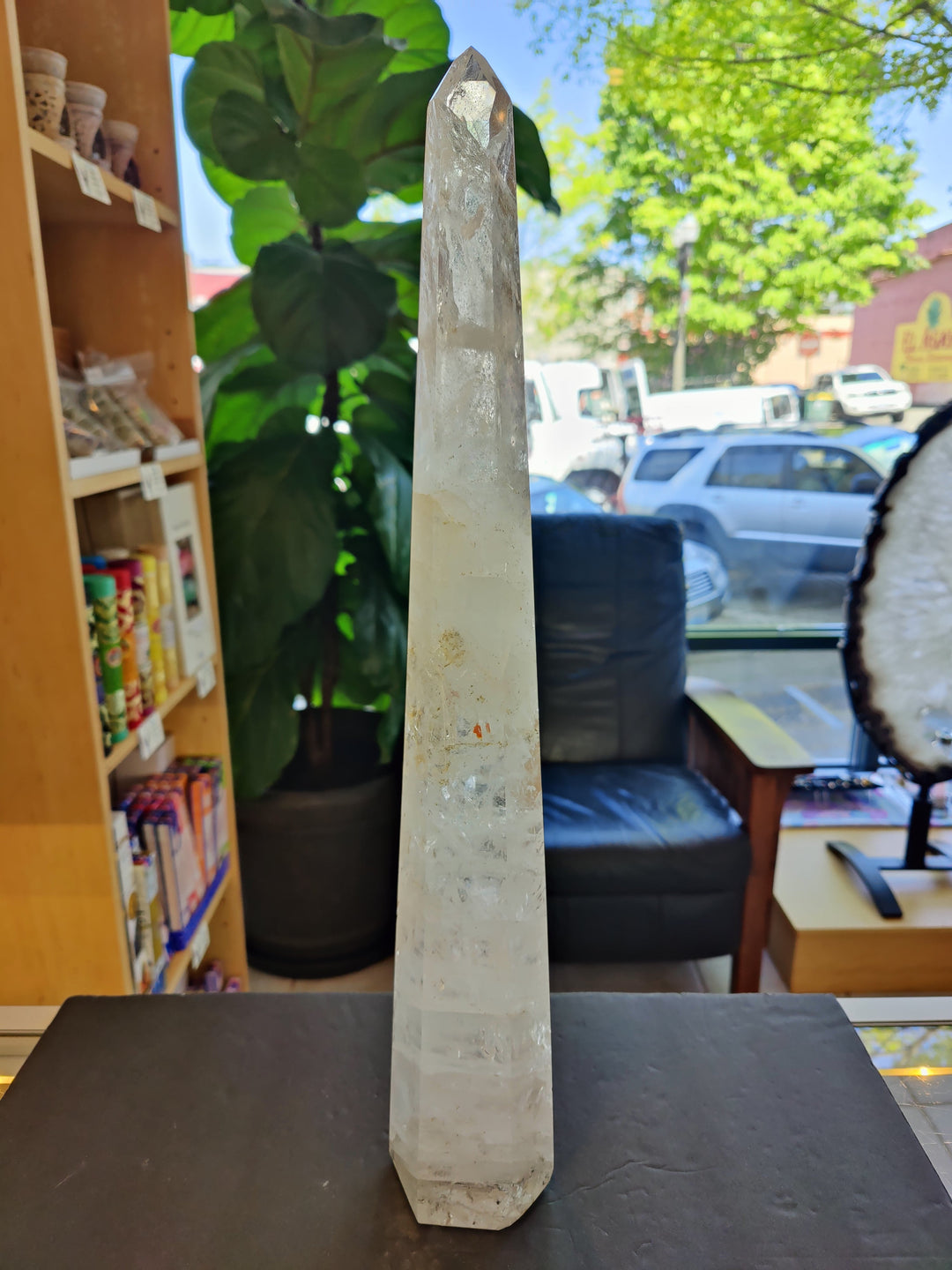 Polished clear quartz obelisk crystal with faceted pointed top on dark tabletop