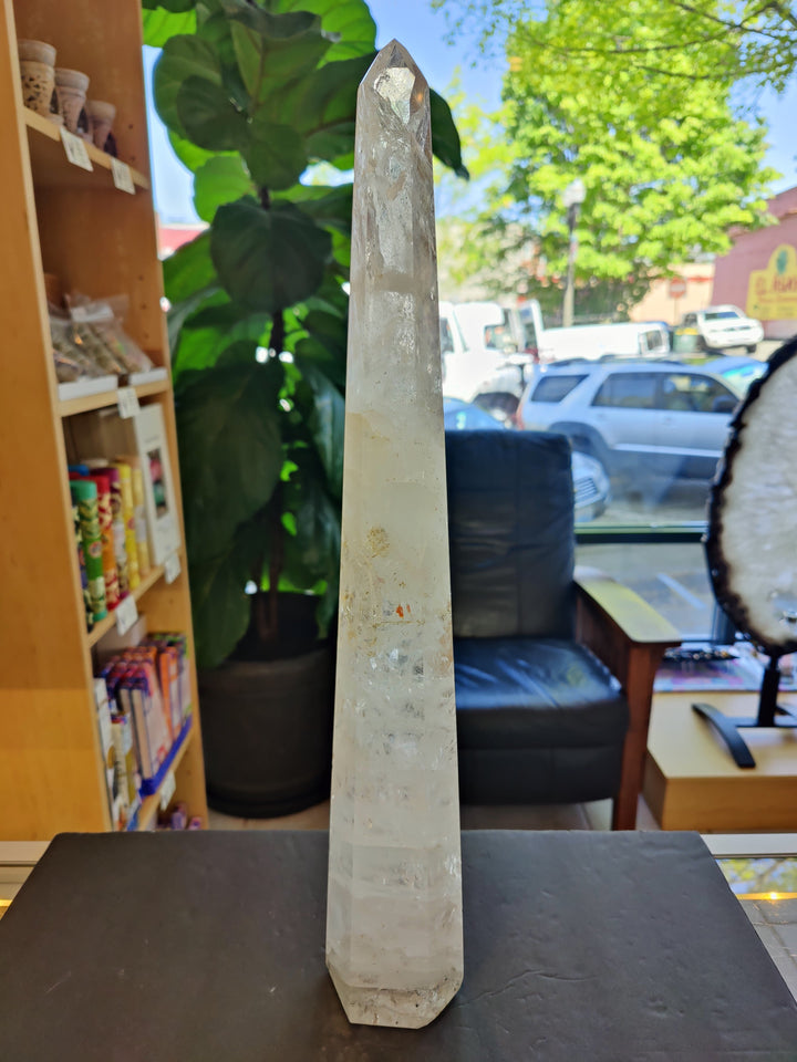 Polished clear quartz obelisk crystal with faceted pointed top on dark tabletop