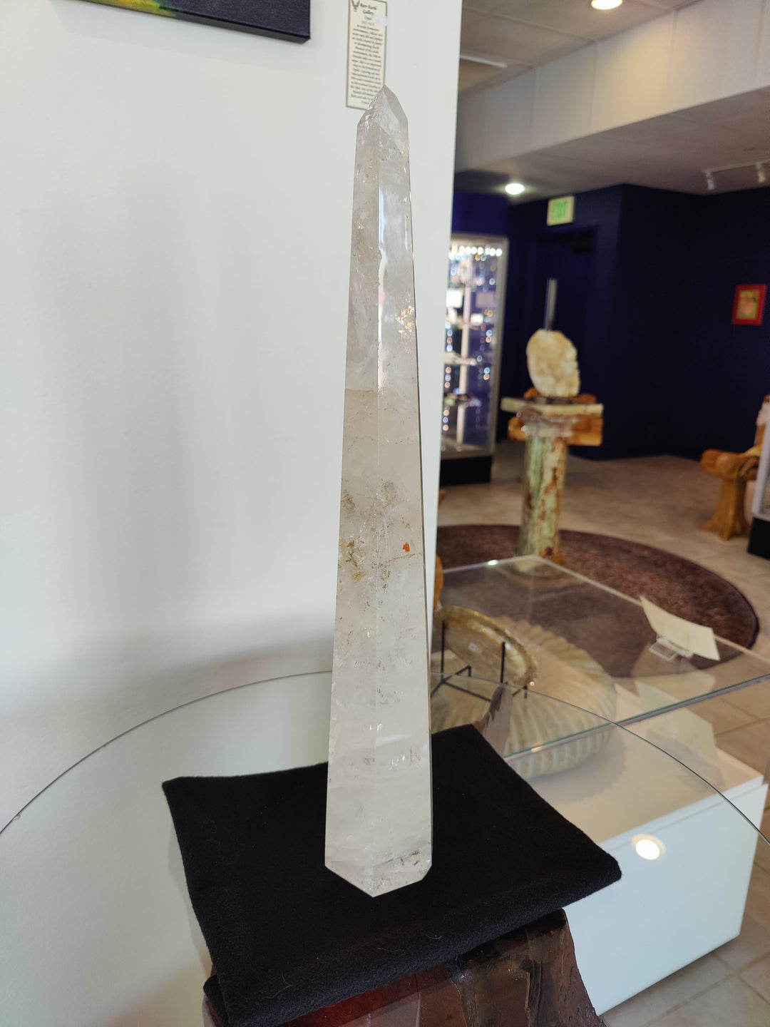Polished clear quartz obelisk sculpture standing on black cushion base