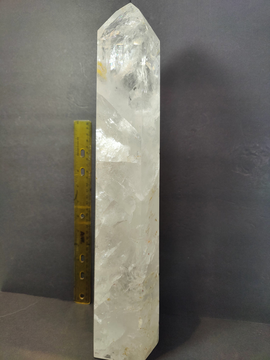 Polished clear quartz obelisk, tall faceted crystal next to yellow measuring ruler