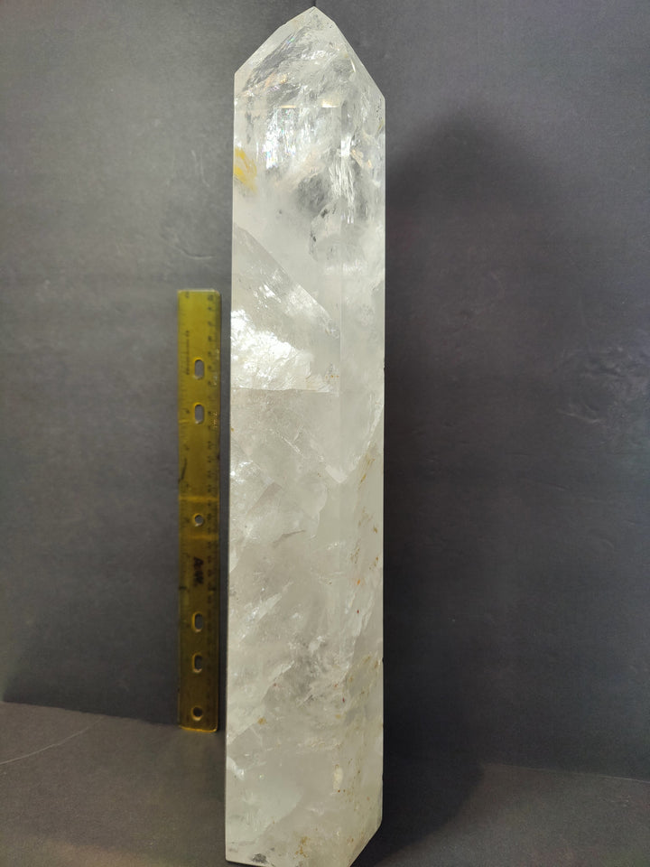 Polished clear quartz obelisk, tall faceted crystal next to yellow measuring ruler