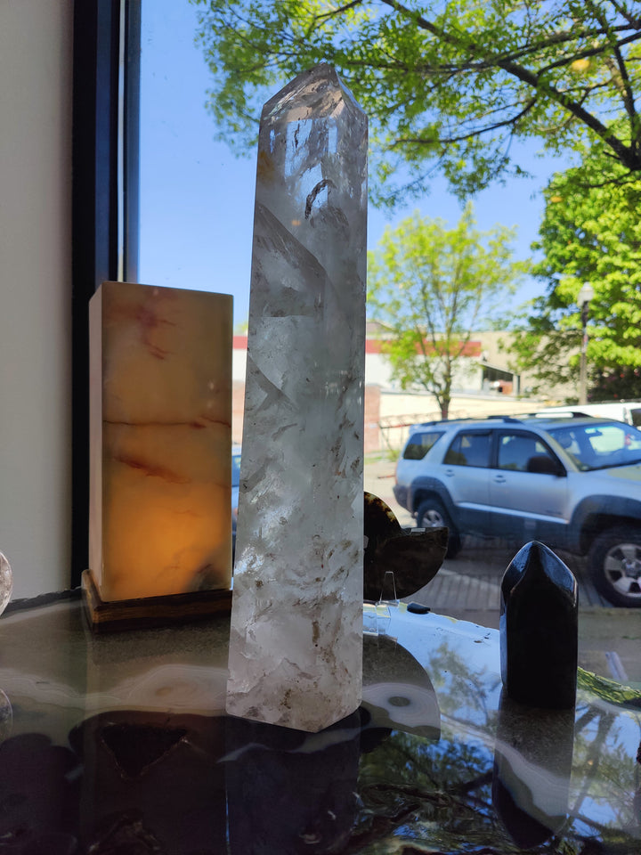 Polished clear quartz obelisk, tall translucent crystal with faceted sides and pointed top