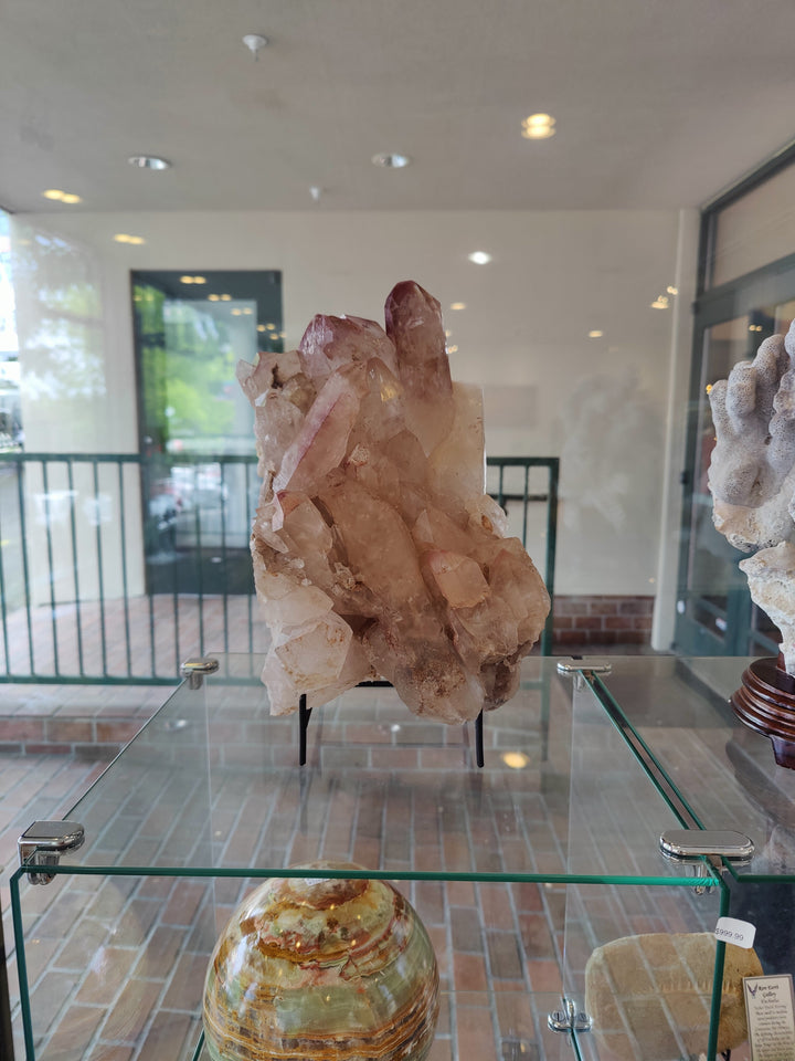 Lithium quartz crystal cluster displayed on glass table with black supports