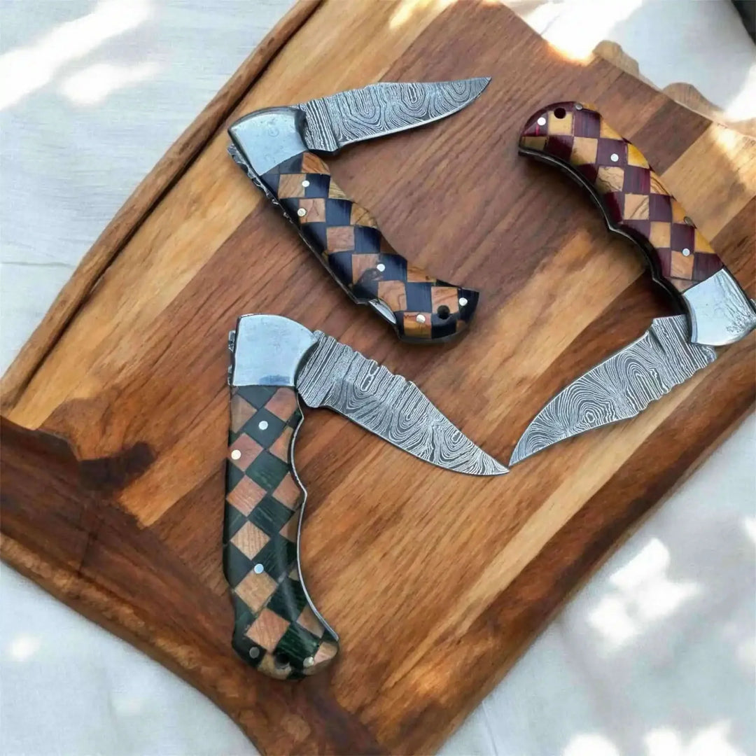 Damascus folding knives with checkered handles on wooden board