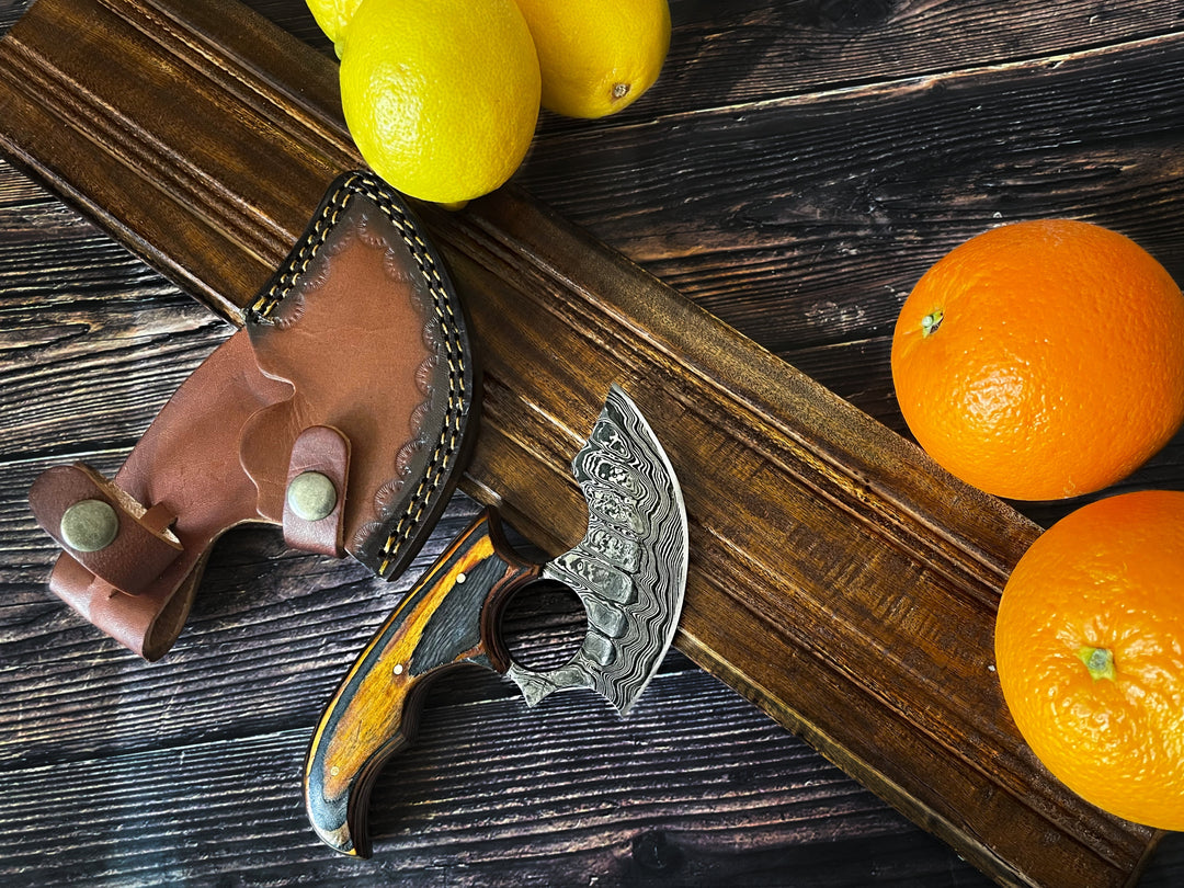 Ulu-style knife with leather sheath and wood handle on rustic wooden surface