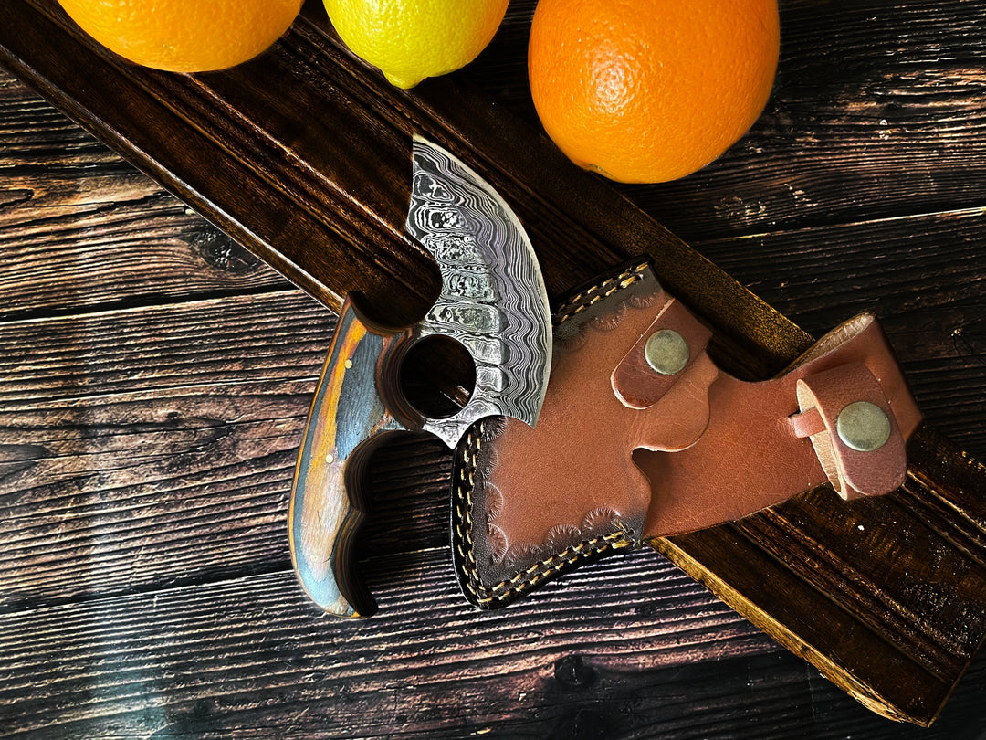 Ulu-style blade with orange wood handle and brown leather sheath on wooden planks