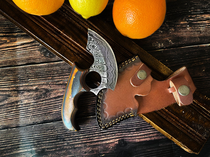 Ulu-style blade with orange wood handle and brown leather sheath on wooden planks