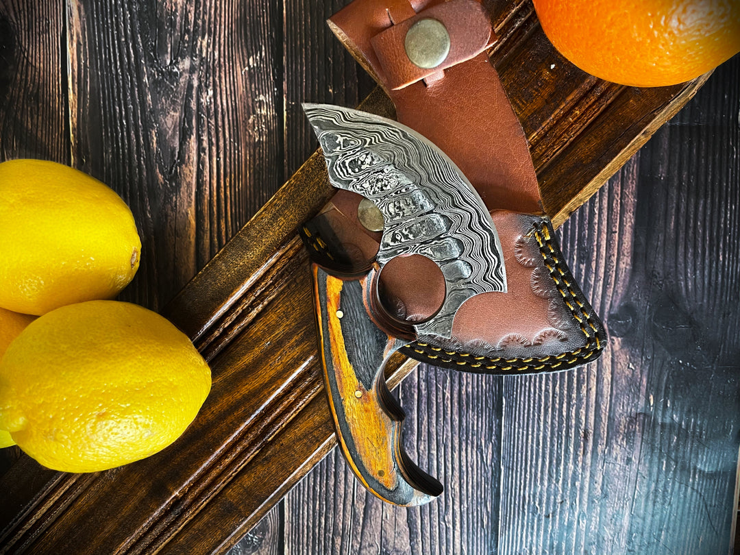 Damascus ulu-style knife with wood handle and brown leather sheath on rustic table