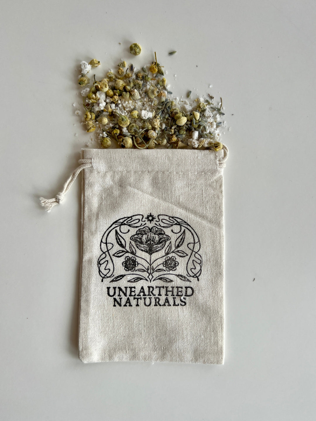 Reusable cotton muslin bath soak bag with drawstring and dried herbs; UNEARTHED NATURALS logo