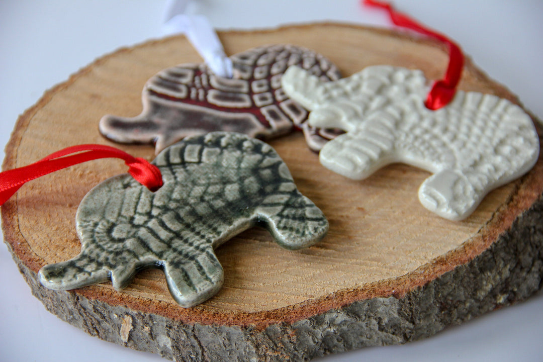 Grey and white elephant ornaments with red ribbon ties on a wood slice