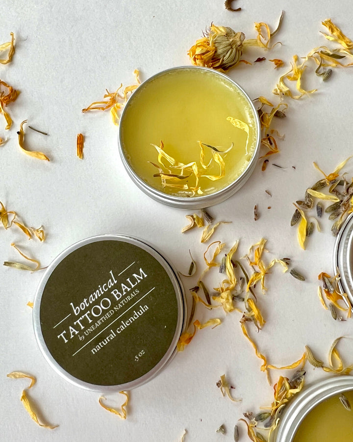 Round balm tins with yellow salve and brown label, with dried petals scattered