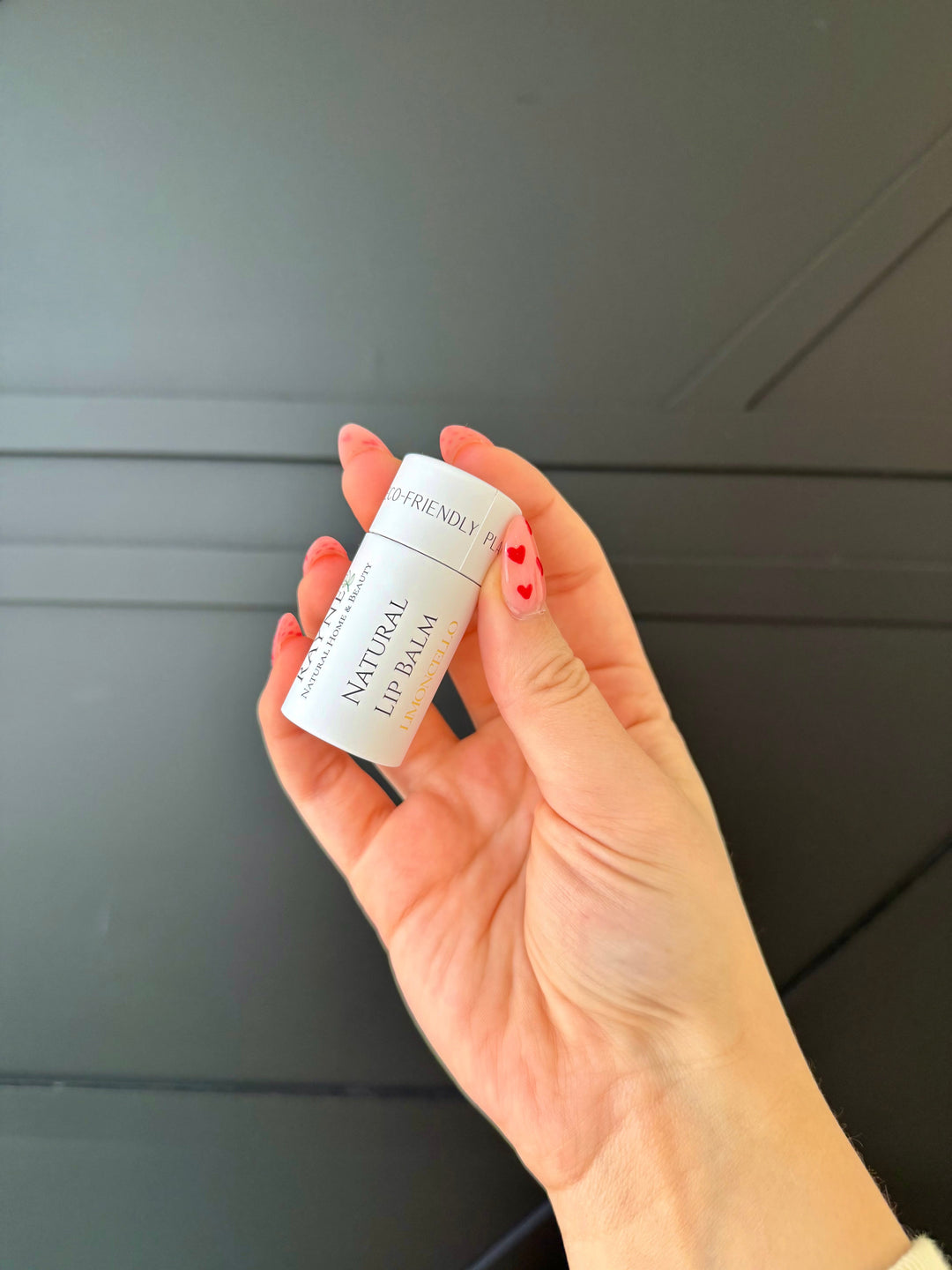 Natural lip balm tube held in hand, white label with small heart icon