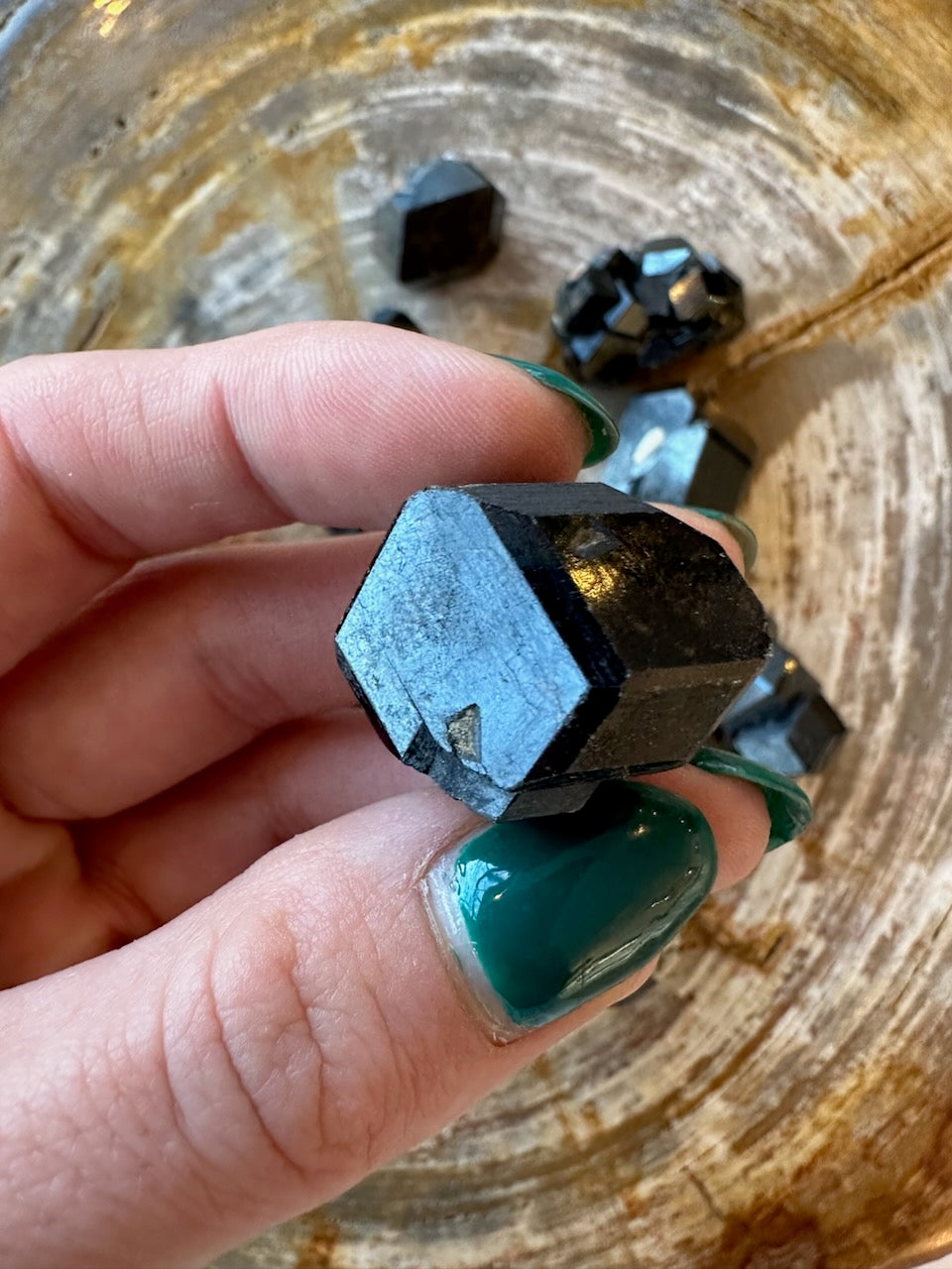 Rough melanite garnet crystal in fingers, dark black with blue reflective surface