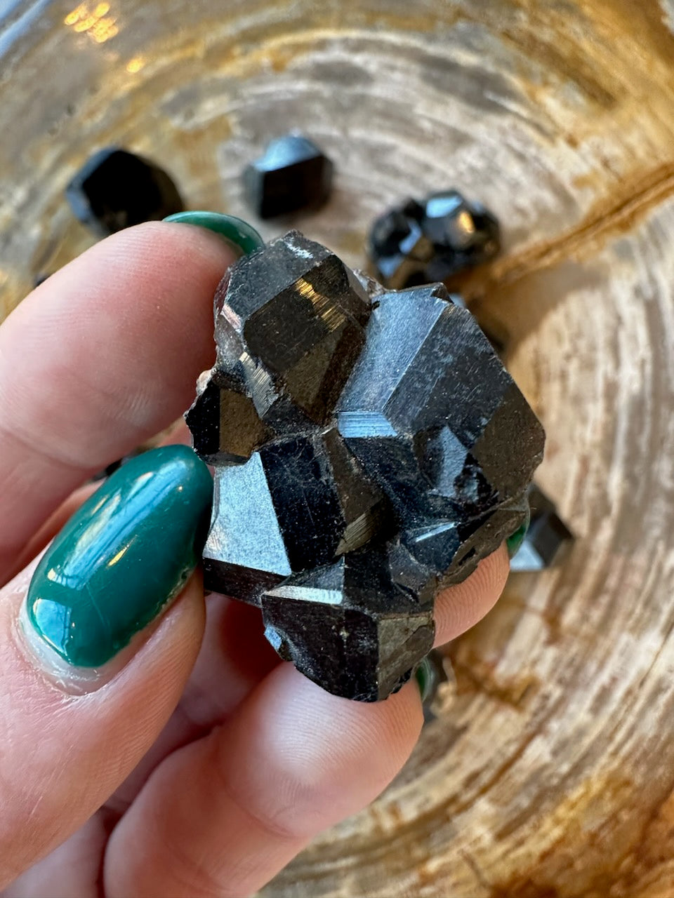 Single rough melanite garnet crystal held in hand, black with blue shimmer