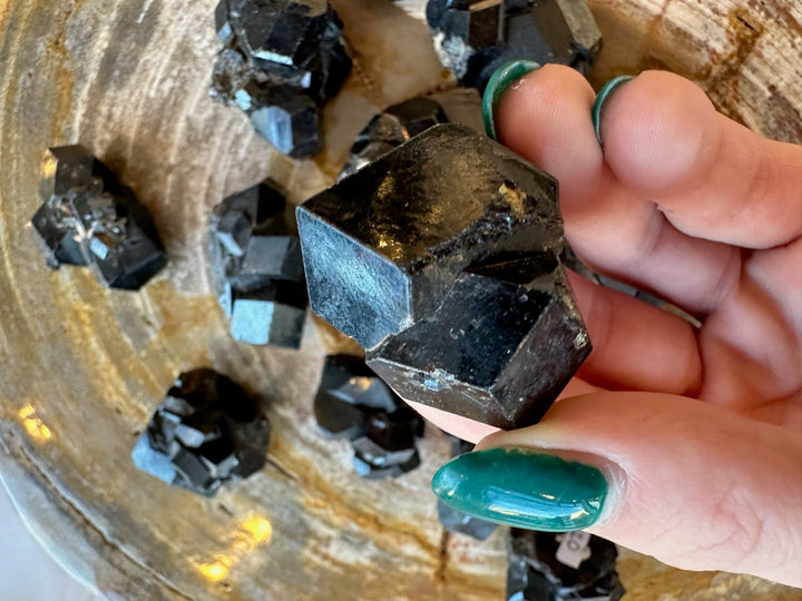 Melanite garnet crystal with black facets and silver-blue reflections, handheld