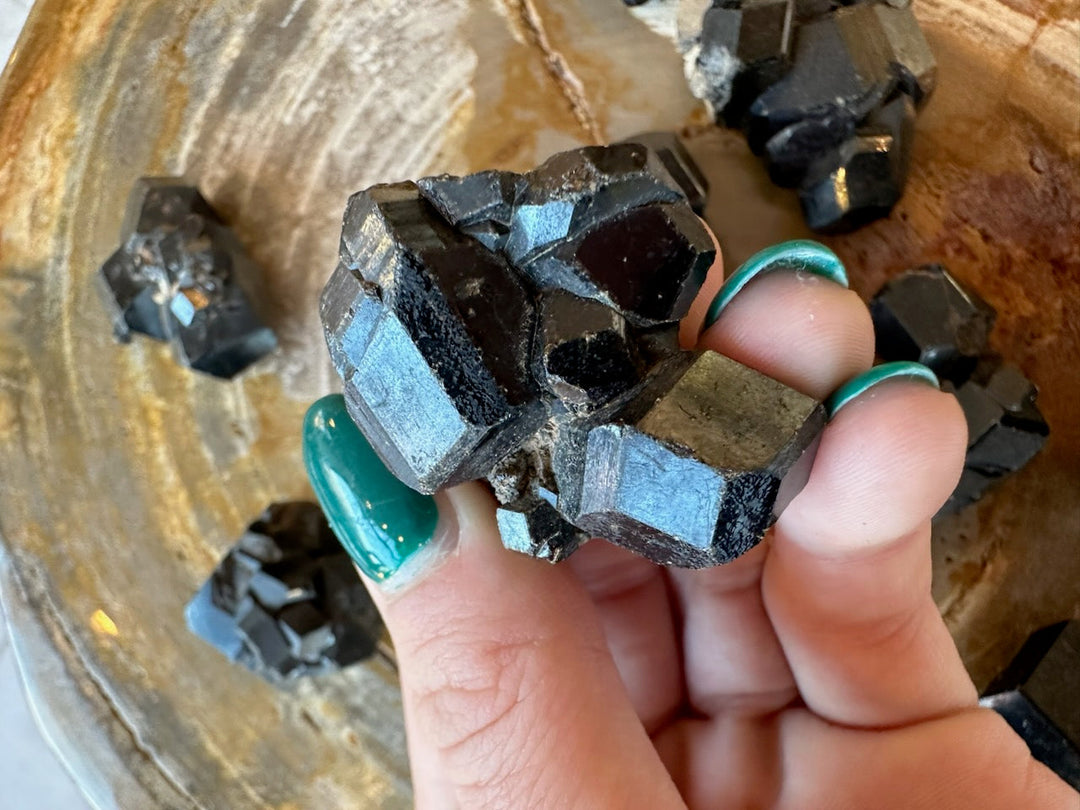 Melanite garnet cube cluster in fingers: dark black crystals with bright silver-blue faces