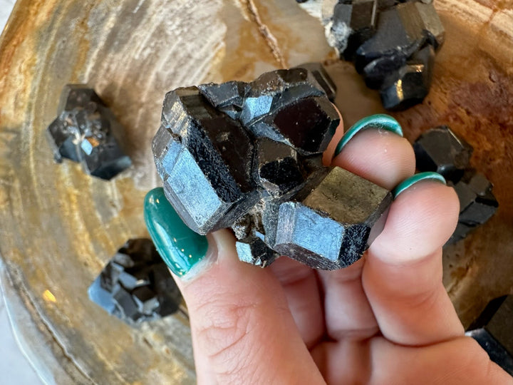 Melanite garnet cube cluster in fingers: dark black crystals with bright silver-blue faces