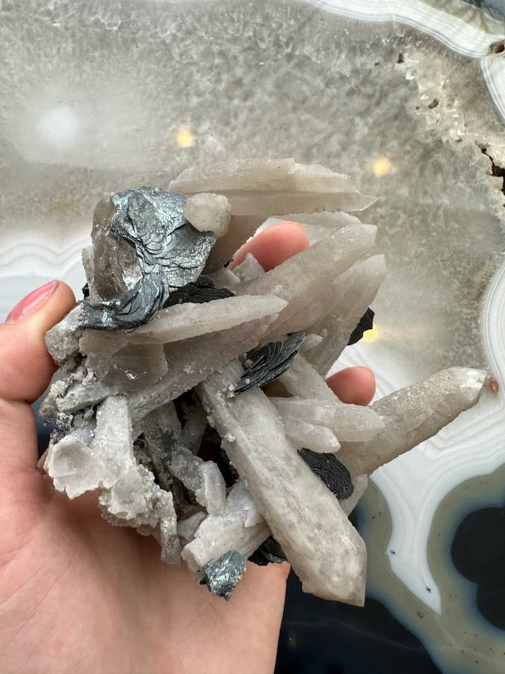 Dogtooth calcite cluster with mica, hand holding pale calcite prisms and dark mica patches