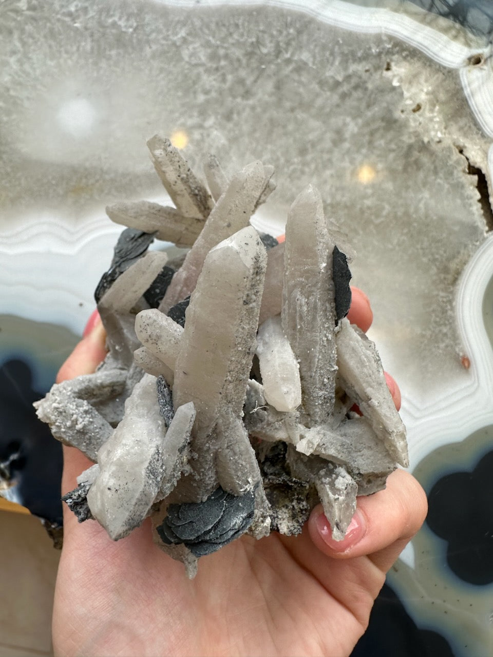 Dogtooth calcite cluster with mica, hand-held pale blades and dark metallic mica streaks