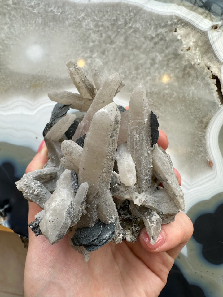 Dogtooth calcite cluster with mica, hand-held pale blades and dark metallic mica streaks