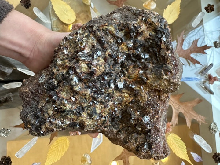 Handheld garnet crystal cluster specimen featuring dense, sparkling silver crystals on dark rock
