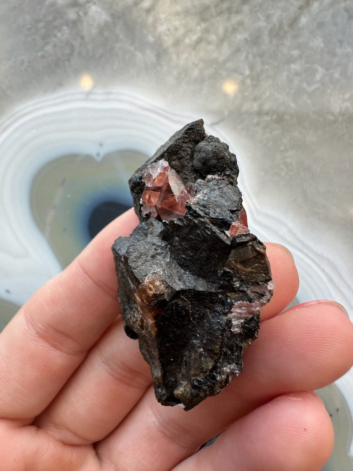 Rhodochrosite crystal cluster on dark rock matrix, red gem cluster close-up