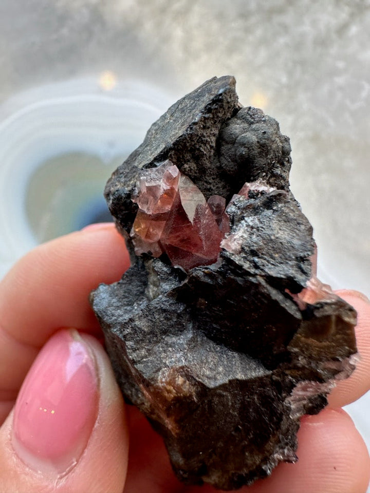 Rhodochrosite crystal cluster on dark rock matrix with small red facets