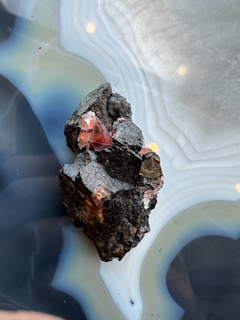 Rhodochrosite crystal cluster on dark rock matrix, red crystals visible