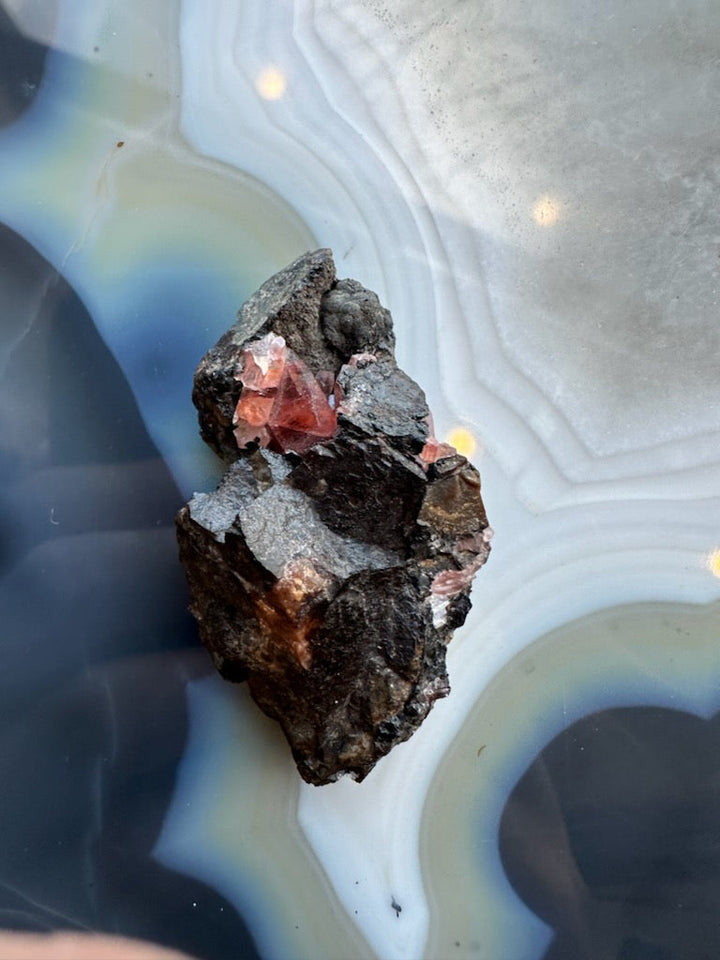 Rhodochrosite crystal cluster on dark rock matrix, red crystals visible