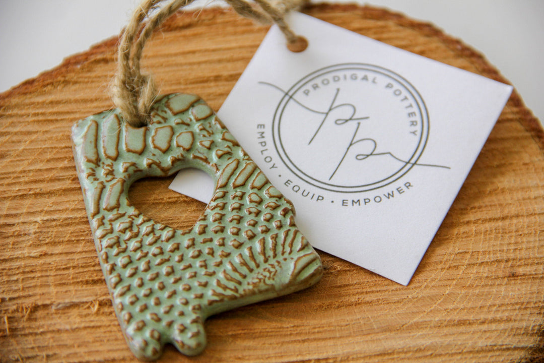 Green glazed letter A ornament with heart cutout, textured finish, on wooden slice