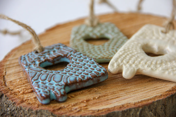 Three glazed letter A ornaments: blue, green, and cream, each with heart cutout